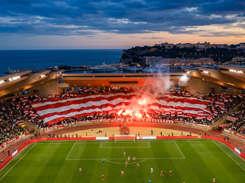 Vue aérienne du Stade Louis II avec drapeaux principautaires rouge et blanc formant une chorégraphie tribune sur la Côte d'Azur